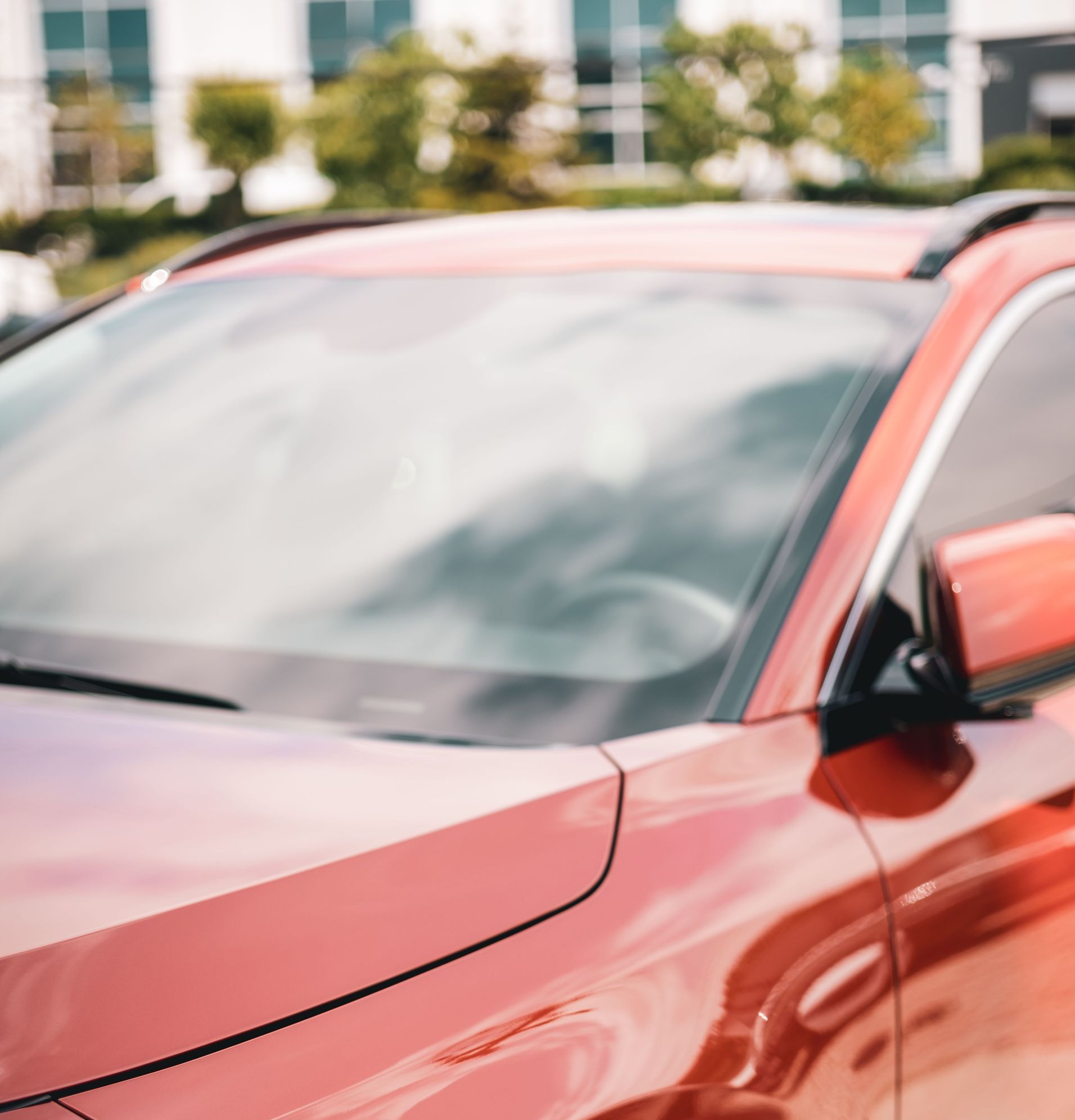 Detailed close-up of a shiny red sports car in bright daylight, showcasing modern design and a polished exterior.